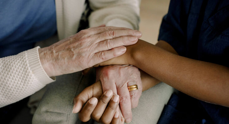 Midsection of senior woman and female healthcare worker with hands stacked at retirement home