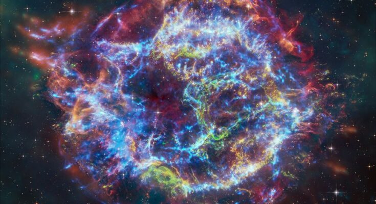 a giant shell of wispy blue, green, yellow and red light glows against the blackness of space in a photo by space telescopes.