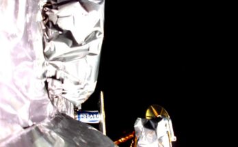photo showing the silvery insulation of a spacecraft and the blackness of space in the background, with a possible sliver of earth in the upper right corner.