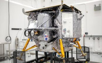 a silver spacecraft sits in a large white-walled room.