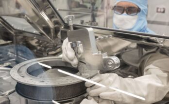 A scientist in clean room suit attaches tool in glove box on asteroid sample capsule