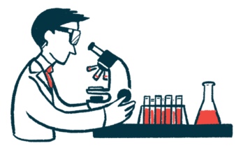 A scientist looks through a microscope on a table with a beaker and test tubes.
