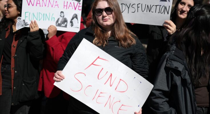 A younger person holds a sign that reads FUND SCIENCE at a national Stand up for Science rally in 2025.
