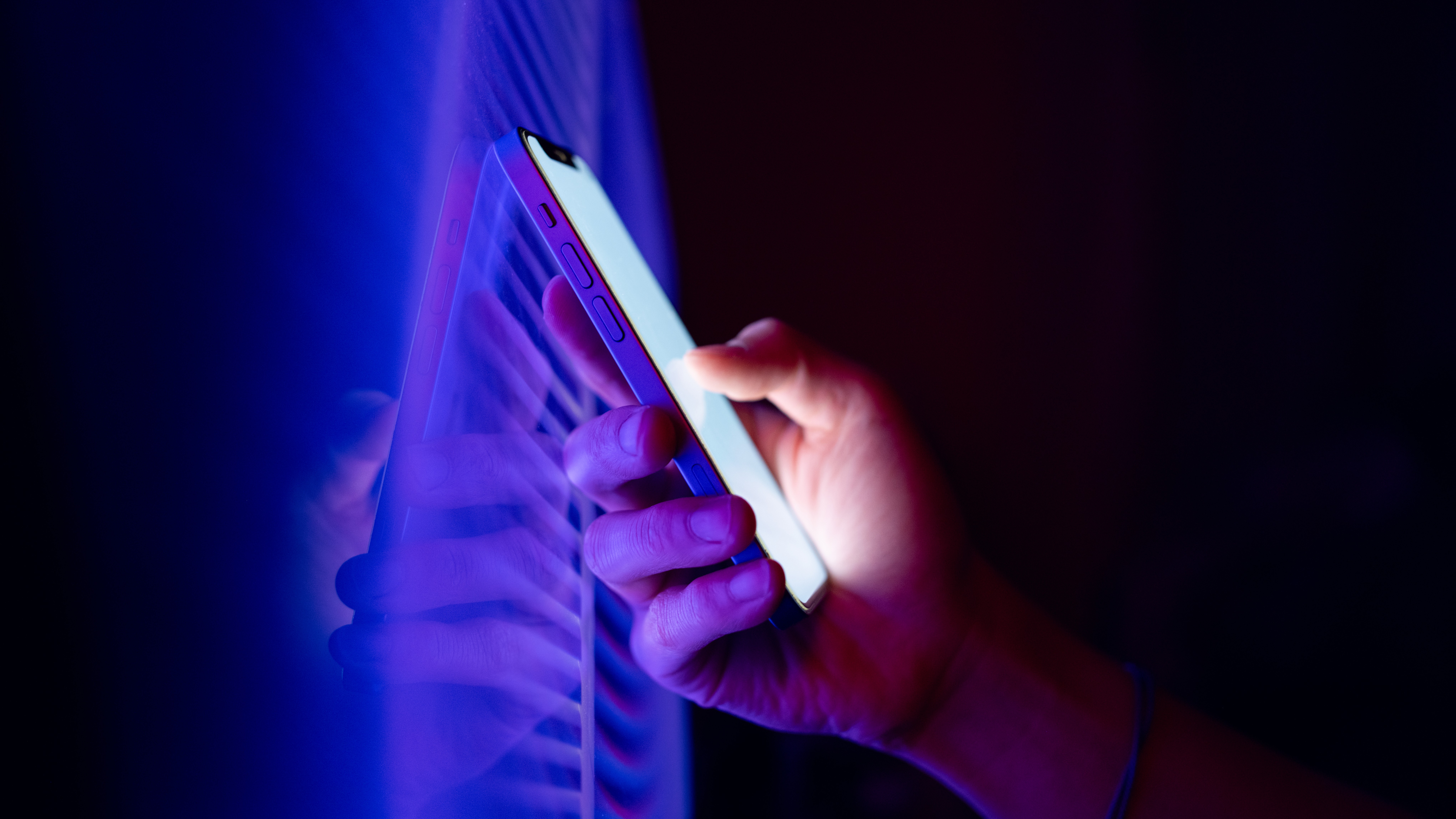 Fotografía Foto de la mano sosteniendo el teléfono frente a la pantalla LED azul.