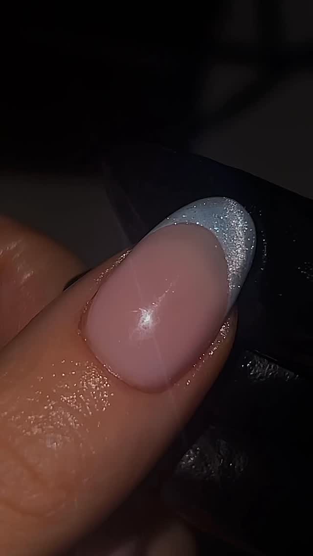 Una foto muy cercana de una uña pintada con una base rosa transparente y punta francesa con brillo plateado por @bambinailss