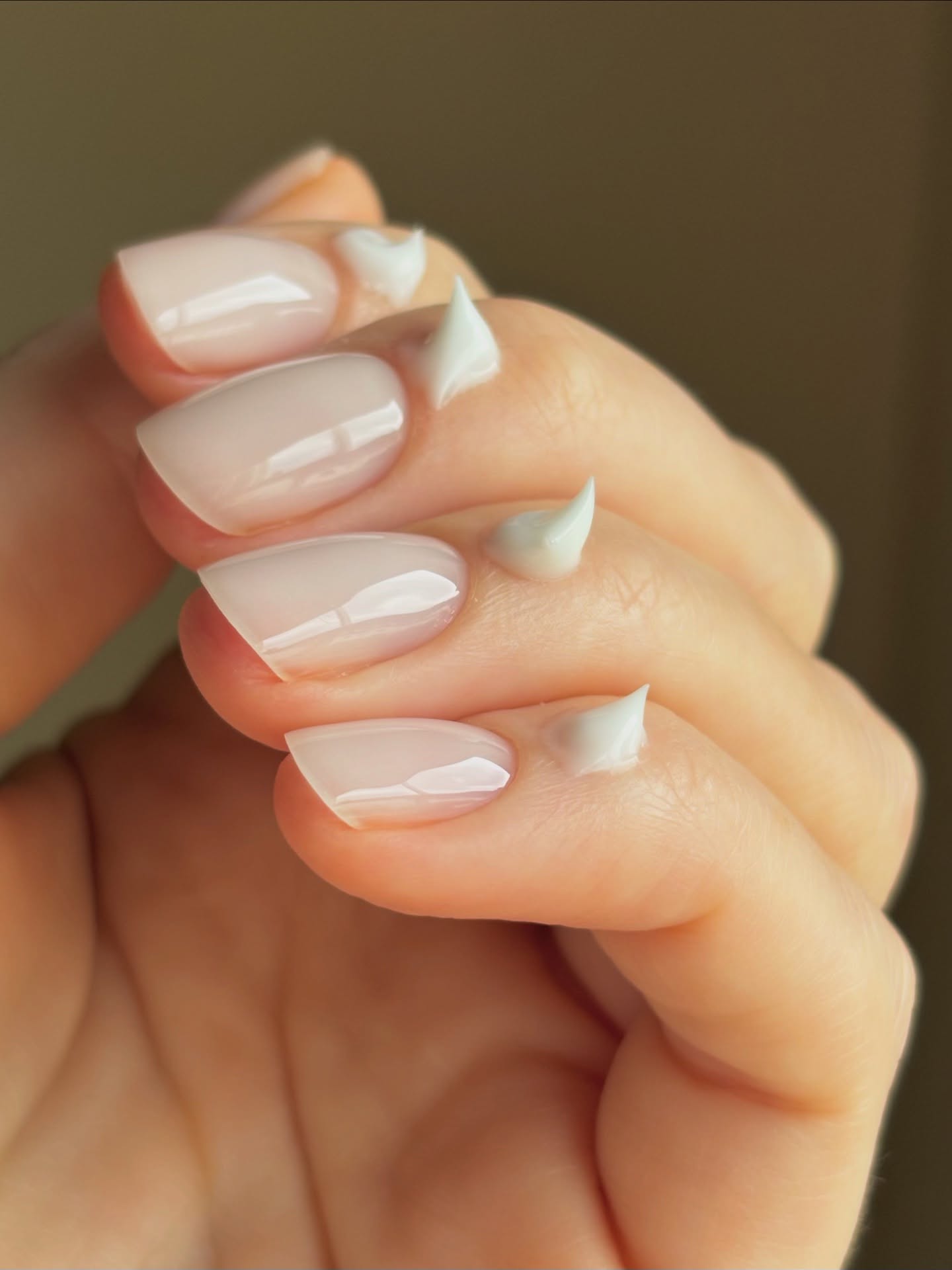 Foto de uñas cortas pintadas completamente de rosa con crema para cutículas recubierta en la base de cada uña.