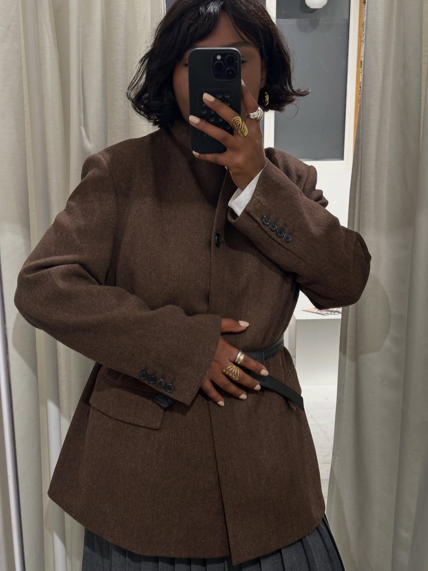 Una foto de @frannfyne tomándose una selfie en el espejo, vestida con una chaqueta marrón y las uñas pintadas de un tono blanco lechoso.