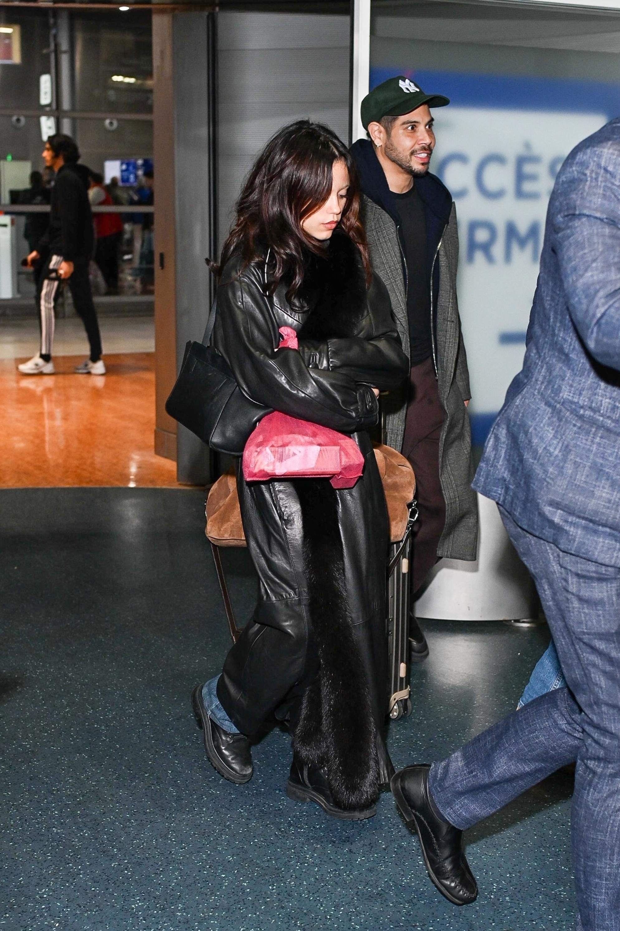 Jenna Ortega viste un abrigo negro de cuero con adornos de piel, jeans y zapatos derby negros.