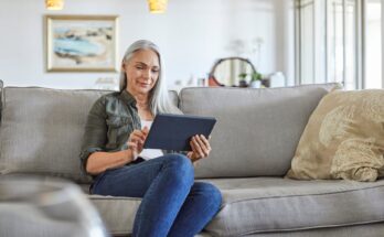 A woman sitting on a couch looking at a tablet.