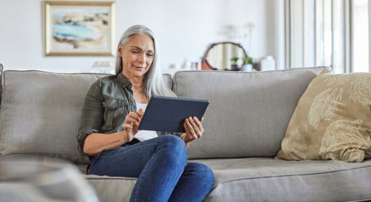 A woman sitting on a couch looking at a tablet.