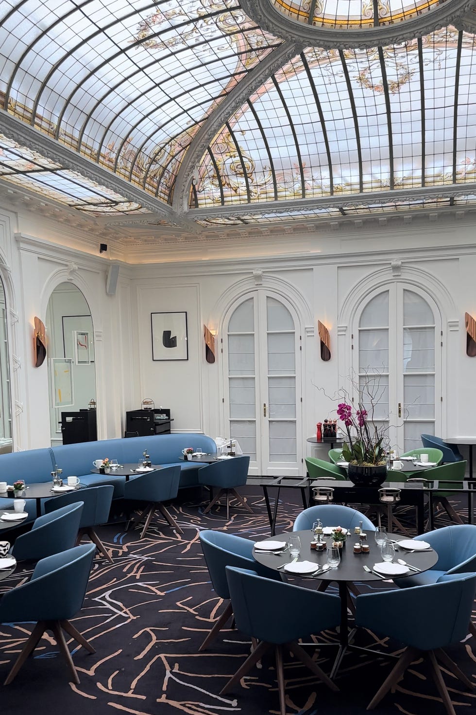 Chez V, un restaurante interior en el Hotel Vernet de París, con sillas de comedor azules y una cúpula de vidrieras en el techo.