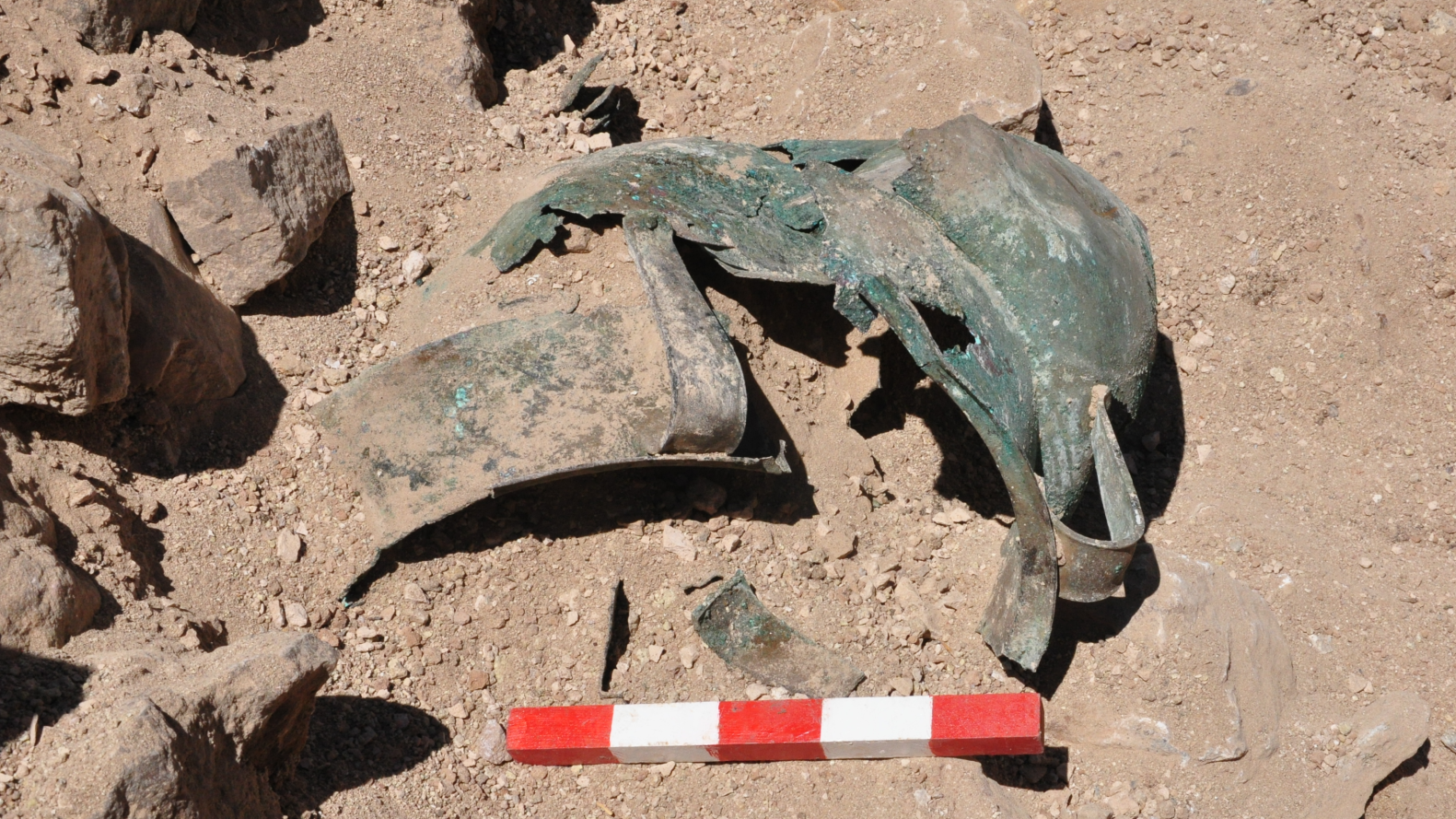 Varias vasijas de bronce asoman entre la tierra roja en una excavación arqueológica