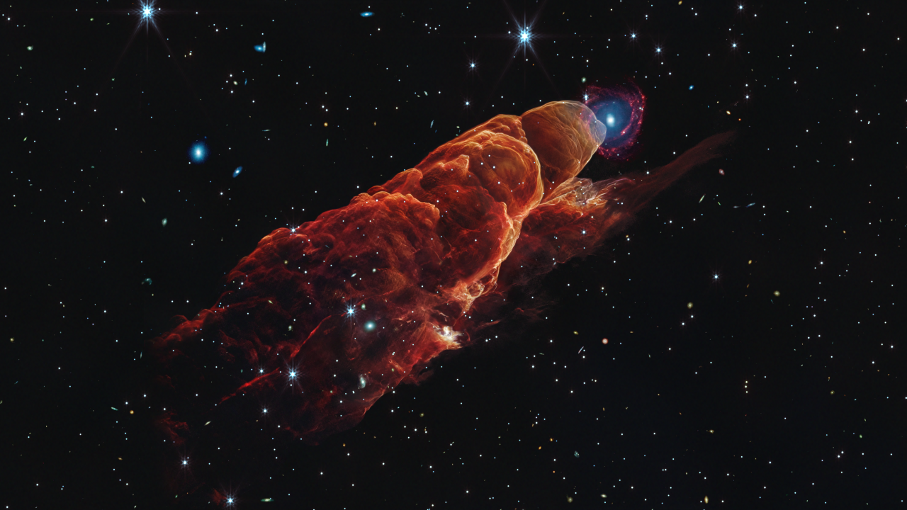 La nube de color rojo anaranjado en forma de cono desde la esquina superior izquierda hasta la esquina inferior derecha se llama Herbig-Harrow 49/50. Esta característica ocupa tres cuartos de la longitud de este ángulo. La esquina superior izquierda de esta característica tiene una punta redondeada y translúcida. Una característica cónica se extiende ligeramente desde la punta redondeada en la parte superior derecha hasta la parte inferior derecha. Bordes redondeados adicionales a lo largo del cono, bordes ondulados y detalles intrincados similares a espuma, así como una vista clara del fondo negro del espacio. En la parte superior izquierda, se superpone con la punta redondeada de Harbig-Harrow 49/50, una galaxia espiral de fondo con un centro concéntrico azul que se desvanece hacia afuera para mezclarse con los brazos espirales rojos. El fondo espacial está salpicado de algunas estrellas blancas y de galaxias blancas más pequeñas, más numerosas y más débiles.